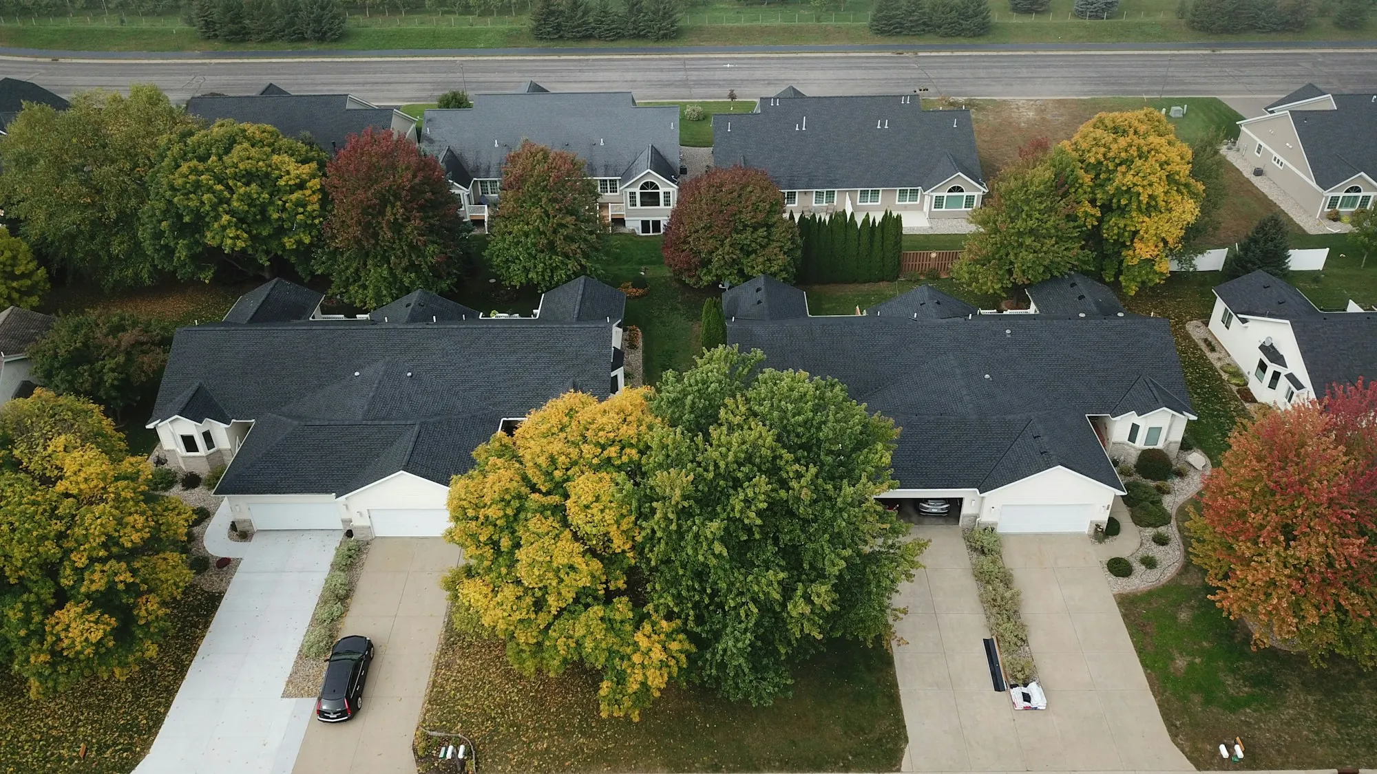 Aerial view of two suburban homes with driveways among autumn trees