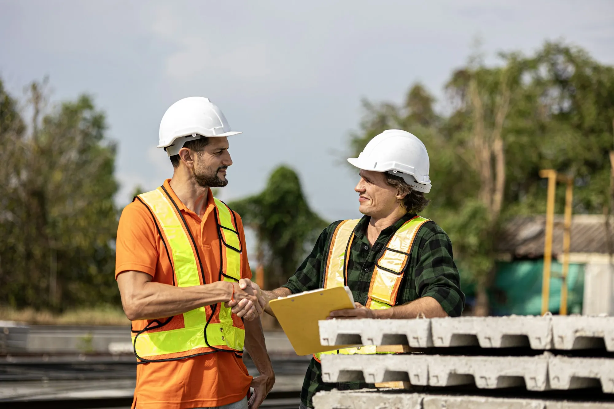 Two workers in hard hats and vests shaking hands at a job site