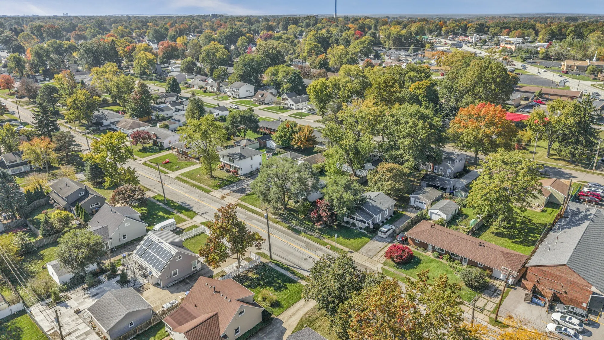 Aerial view of suburban streets and small homes in autumn, one roof covered in solar panels